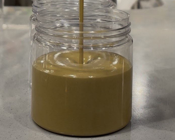 Pistachio spread flowing into a clear jar during filling